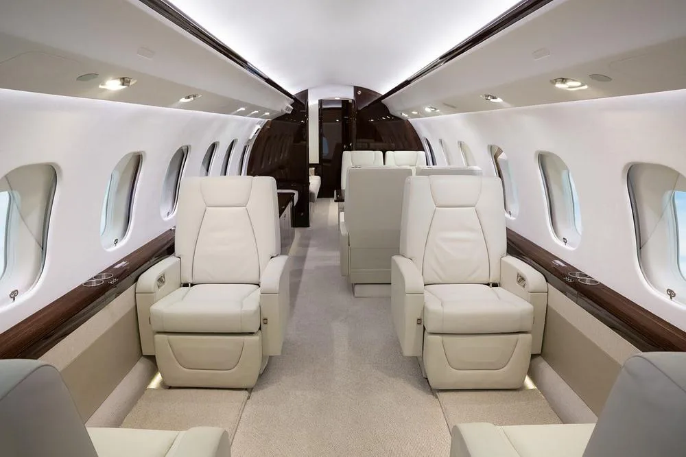 A view of a luxurious aircraft cabin interior with light-colored leather seats and dark wood accents.