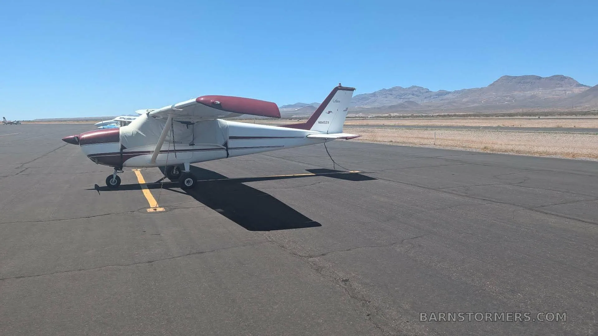A side-rear view of a white and maroon single-engine aircraft with registration N8452X, parked on an airfield.