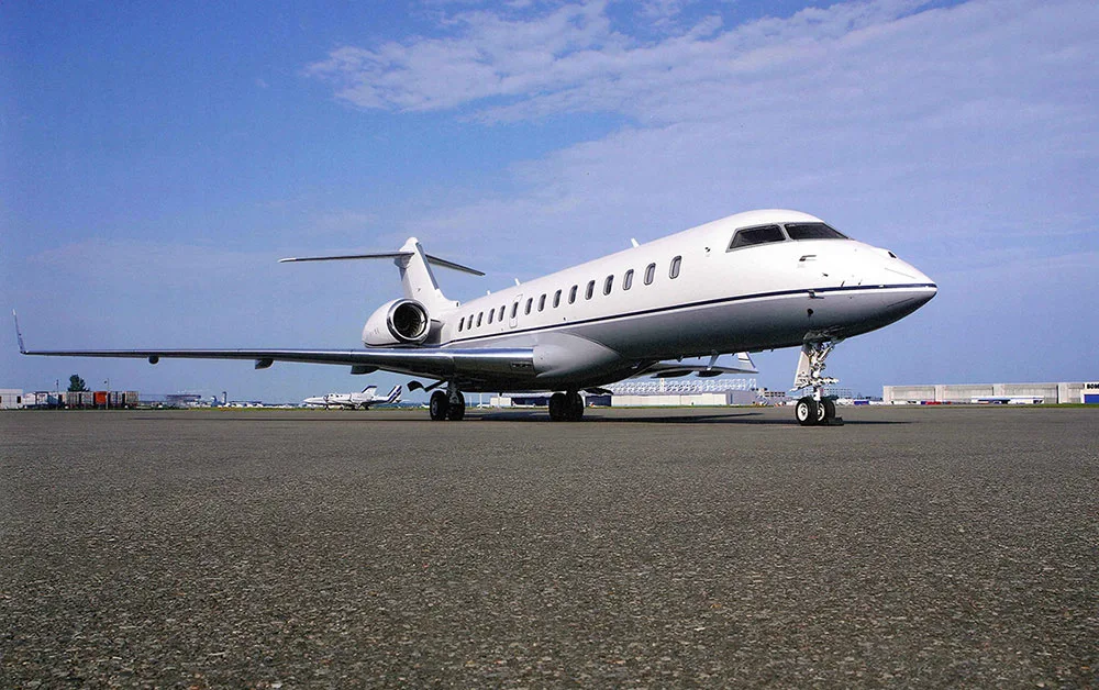 A white Bombardier Global business jet is parked on an airport tarmac under a clear blue sky.