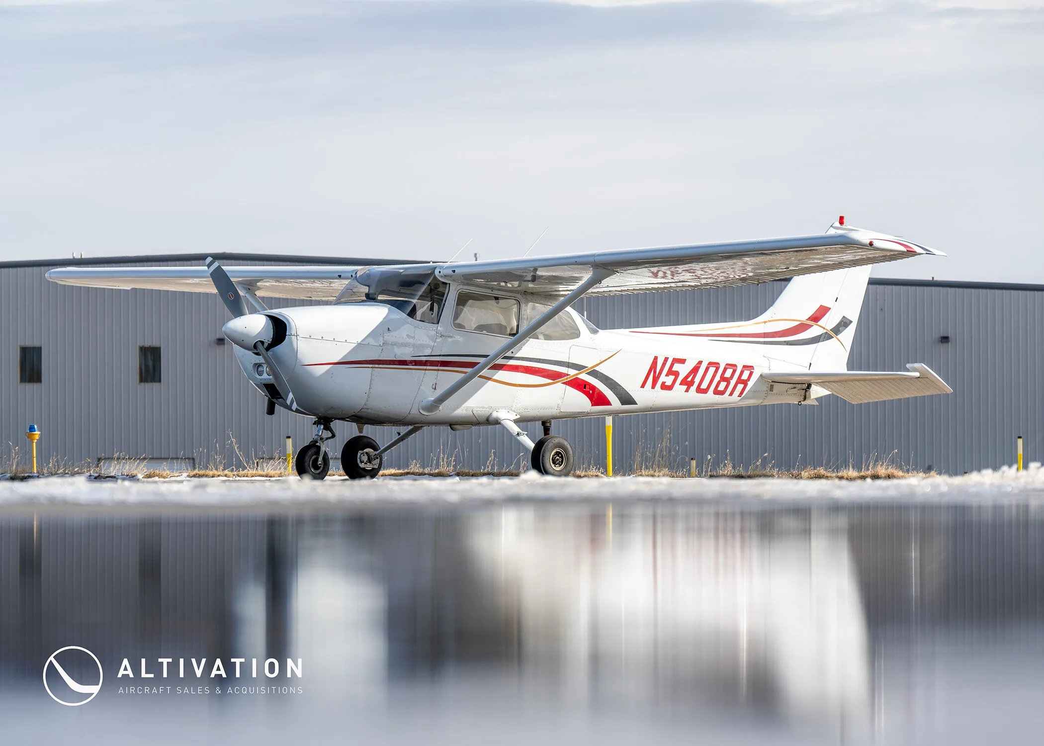 A white Cessna 172 with red and black stripes, registration N5408R, parked on an airfield with a slight reflection.
