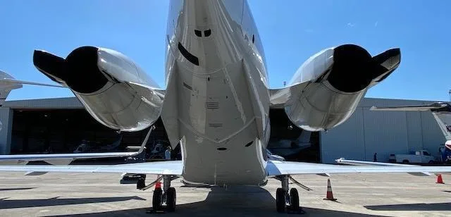 A low-angle rear view of a white business jet showing its two engines and landing gear on the tarmac.