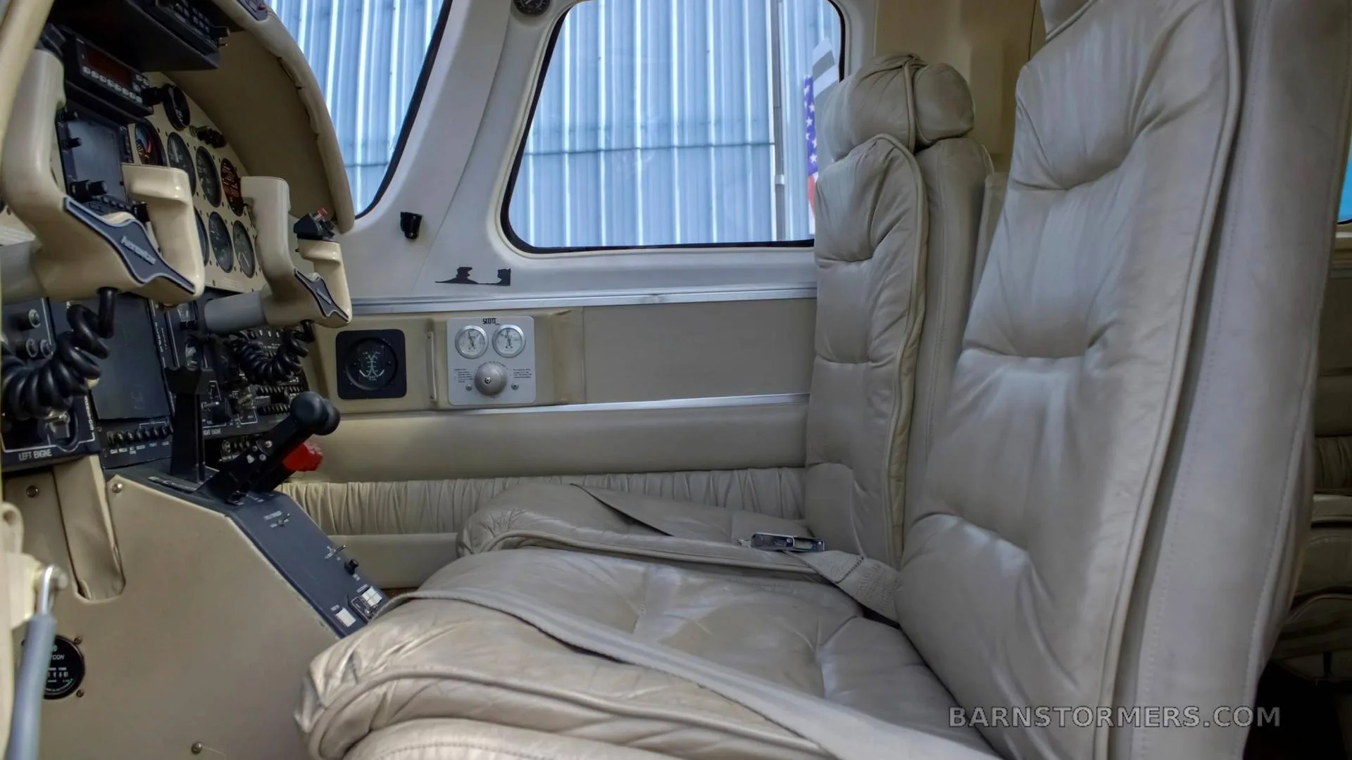 View of the aircraft's light beige leather front passenger seats and a partial view of the cockpit from the cabin.