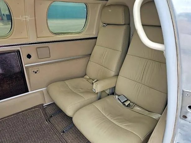 A view of two tan leather passenger seats in the aircraft cabin, showing the carpeted floor and side panel.