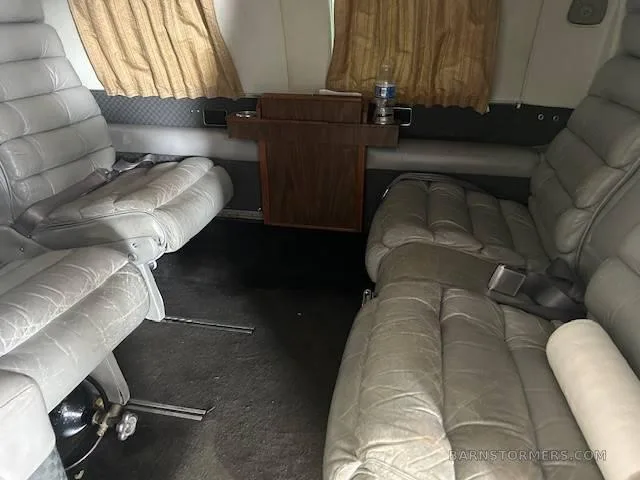 The aircraft's interior cabin with grey leather seats and a small wooden table between them.