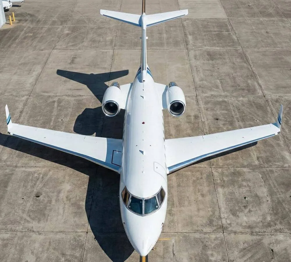 Overhead view of a white business jet with blue and grey stripes parked on the tarmac.