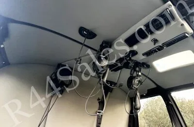 The grey ceiling and overhead panel of a helicopter cabin with communication headsets hanging down.