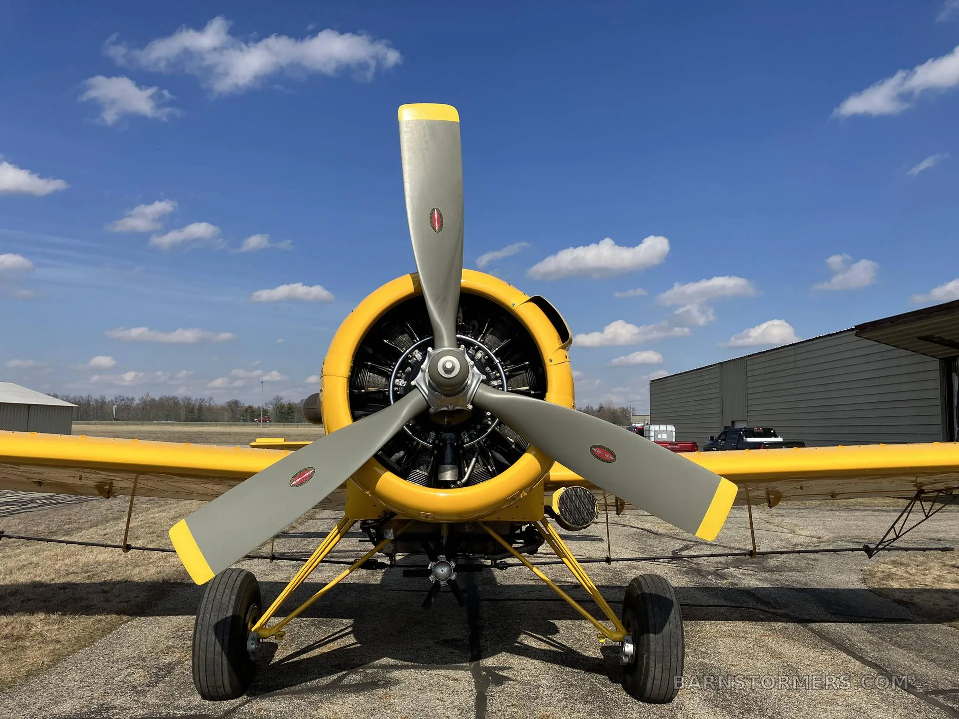 A head-on view of a yellow agricultural aircraft, highlighting its large propeller and radial engine.