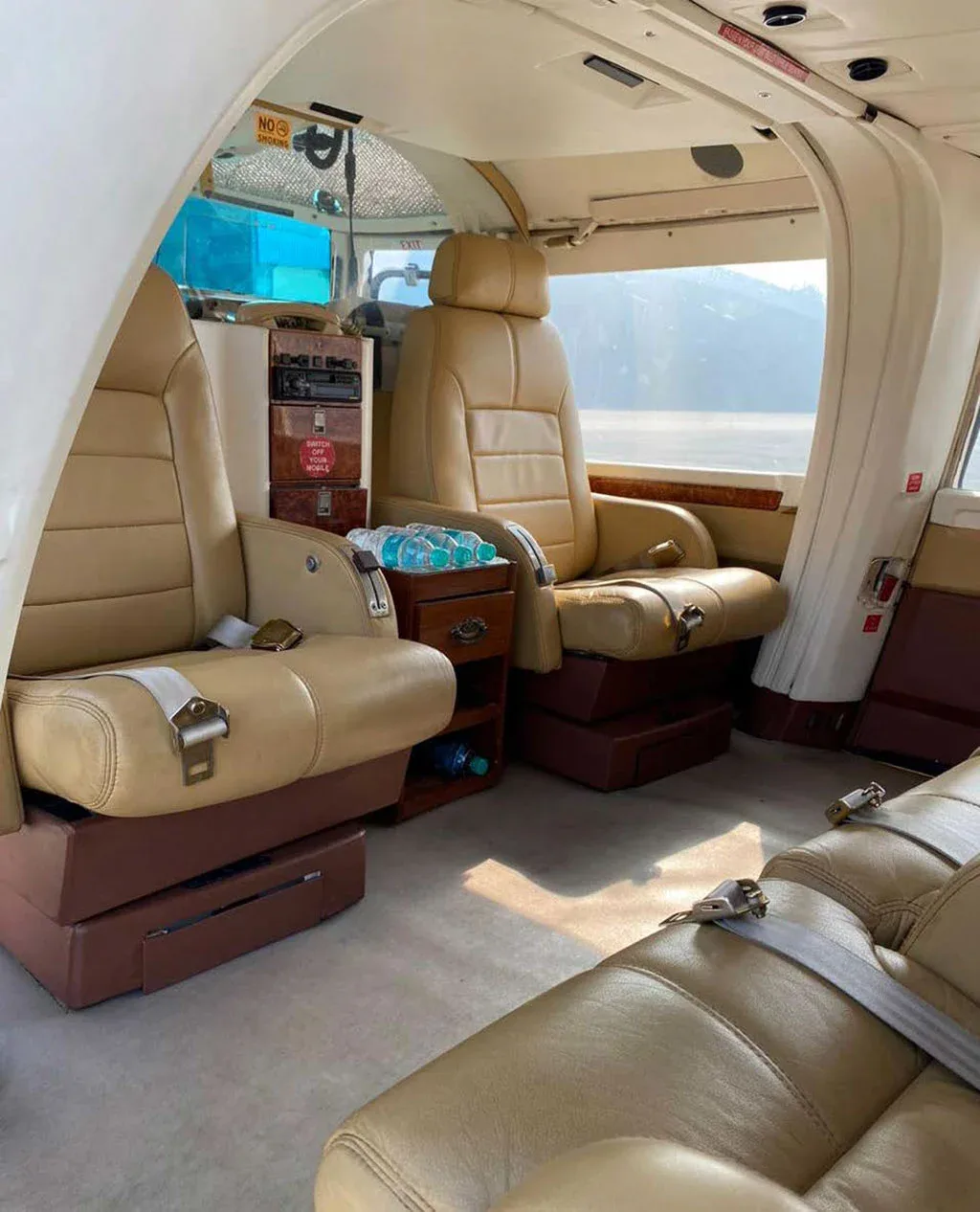 A view of the tan leather interior cabin of a helicopter, showing multiple seats and a small cabinet with bottled water.
