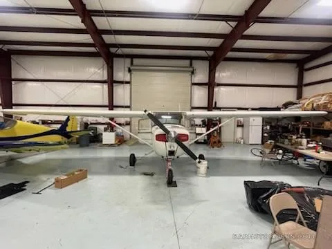 A white Cessna 150/152 type aircraft with a red propeller spinner, registration N10946, is parked head-on in a hangar.