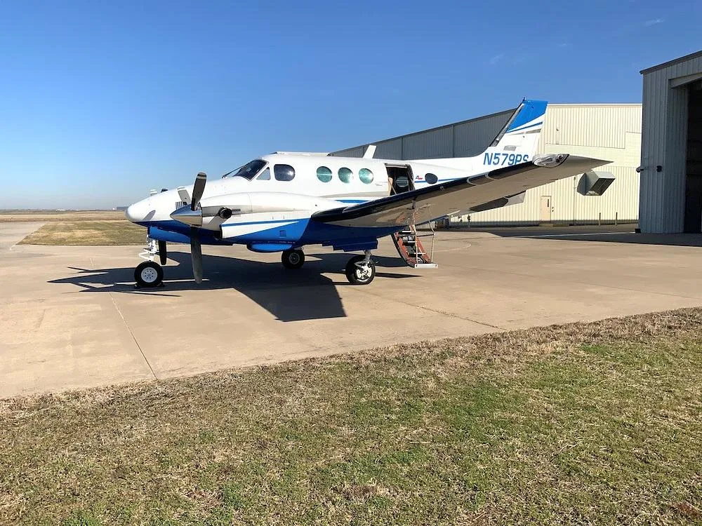 A white and blue twin-engine turboprop aircraft, N579PS, parked on an airfield with its passenger door open.