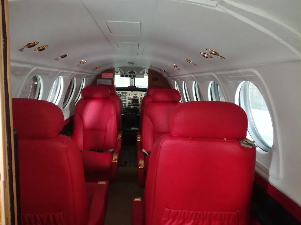 A view down the aircraft cabin aisle showing multiple rows of red leather seats.