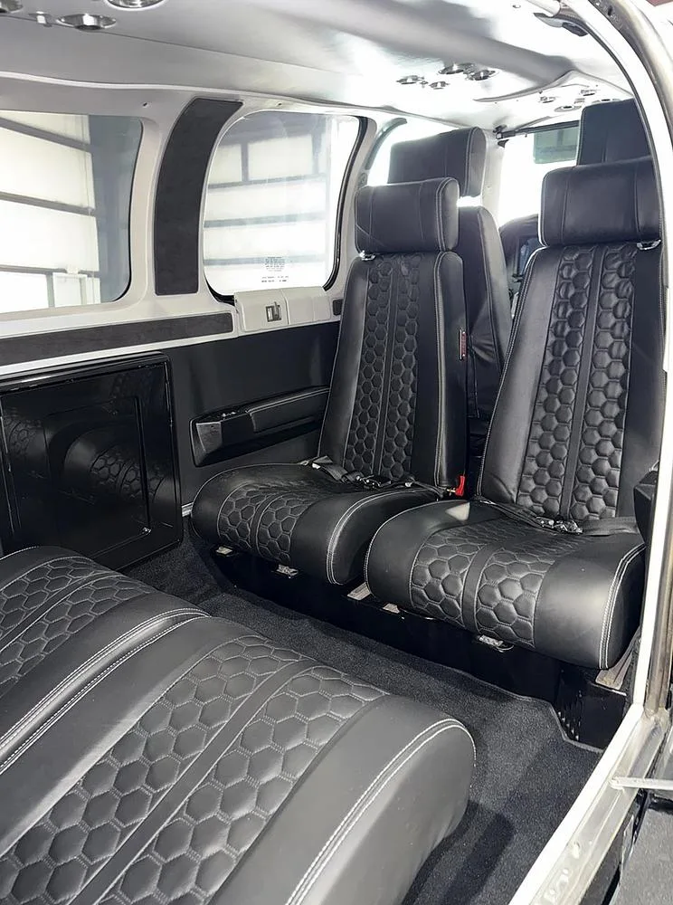The black leather interior of an aircraft cabin, showing two rows of seats with hexagonal stitching.