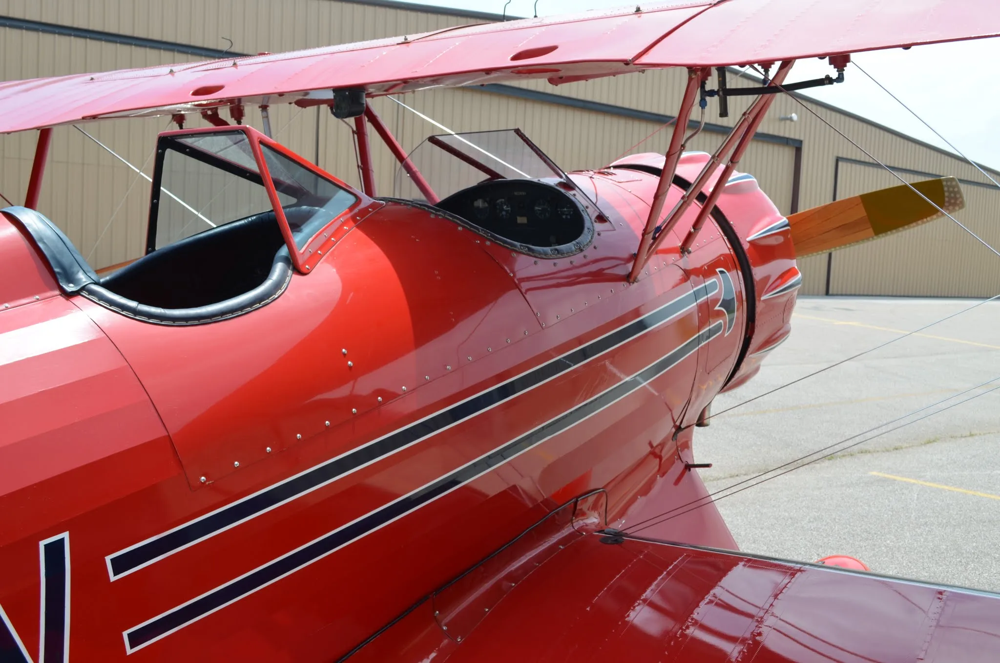 A close-up view of the red biplane's front fuselage, cockpit, and propeller, showing black stripe details.