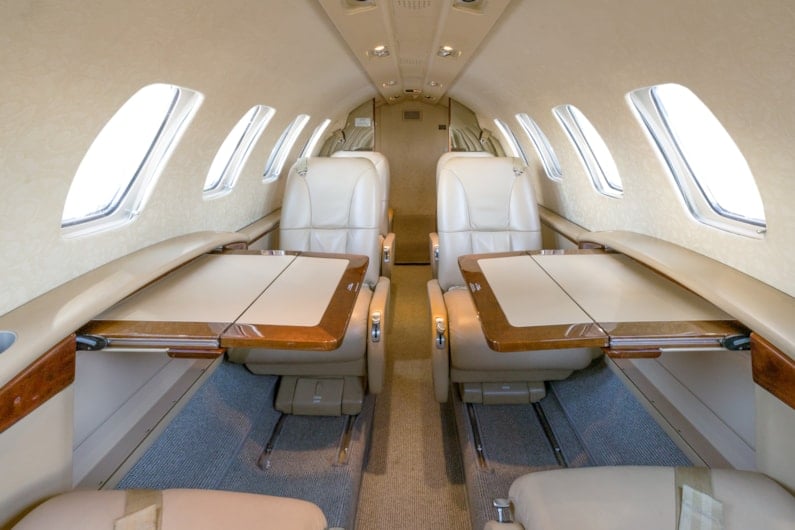Interior view of an aircraft cabin with leather seats and fold-out tables.