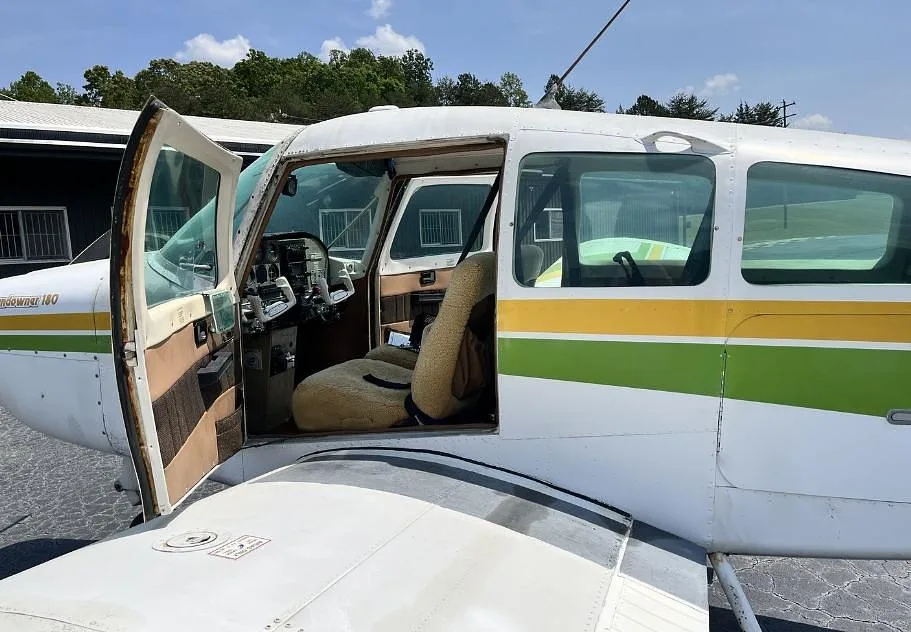 View into the cabin of the Beechcraft Sundowner 180 with the door open, showing a tan seat and part of the cockpit.