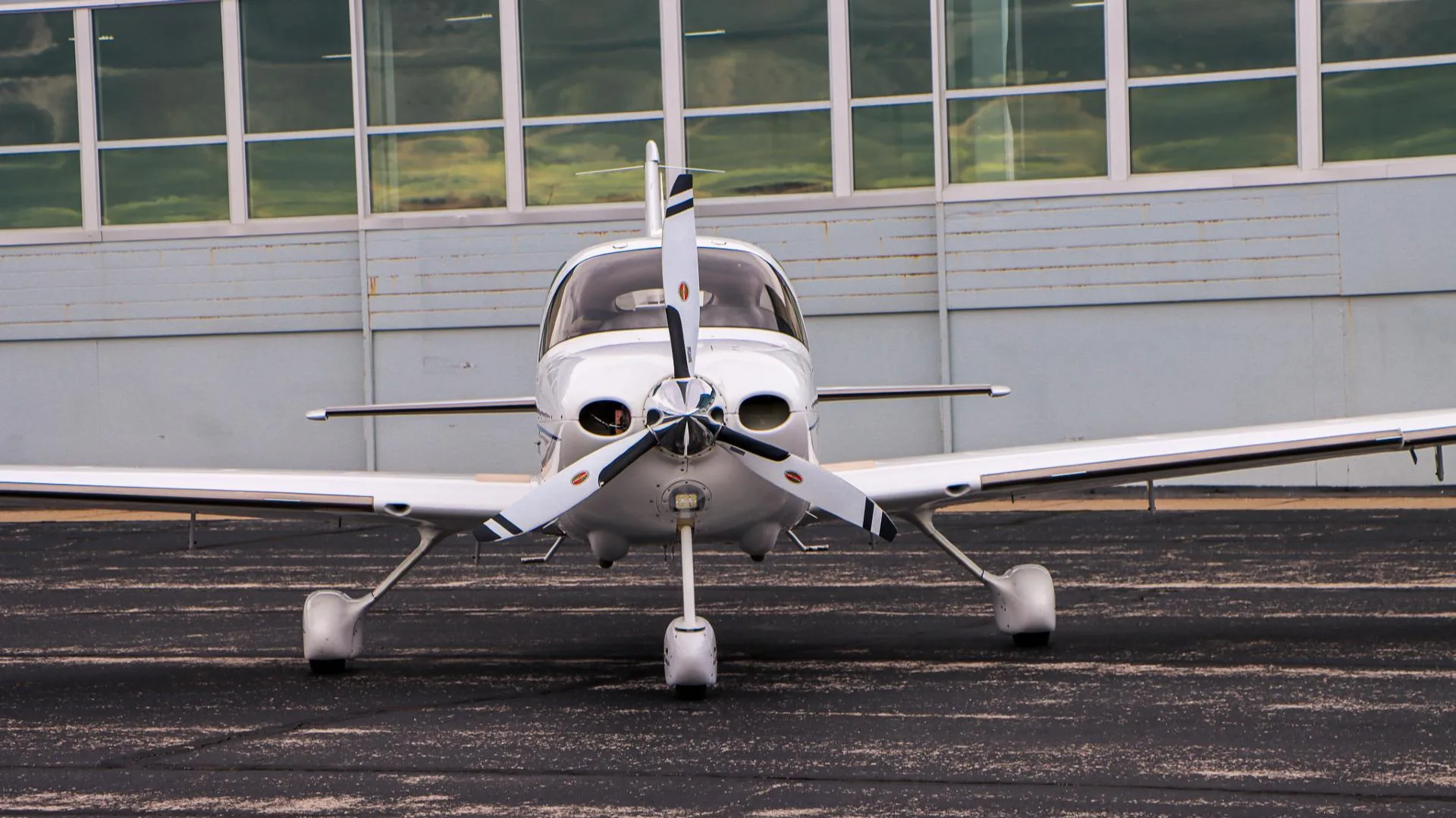 A close-up front view shows the three-bladed propeller and nose of a white Cirrus aircraft.