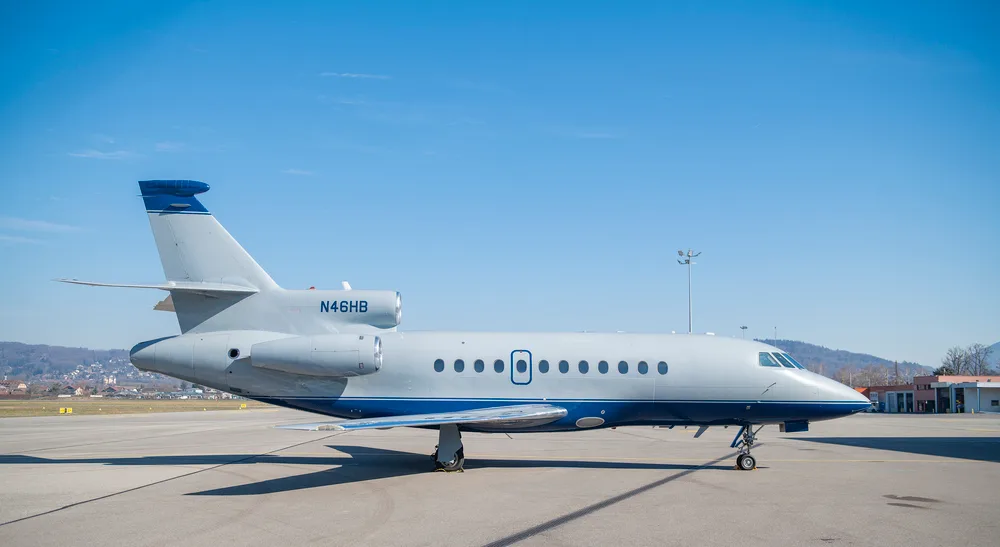 A Dassault Falcon 900EX business jet, registration N46HB, in white and blue livery, parked on an airport tarmac under a clear blue sky.