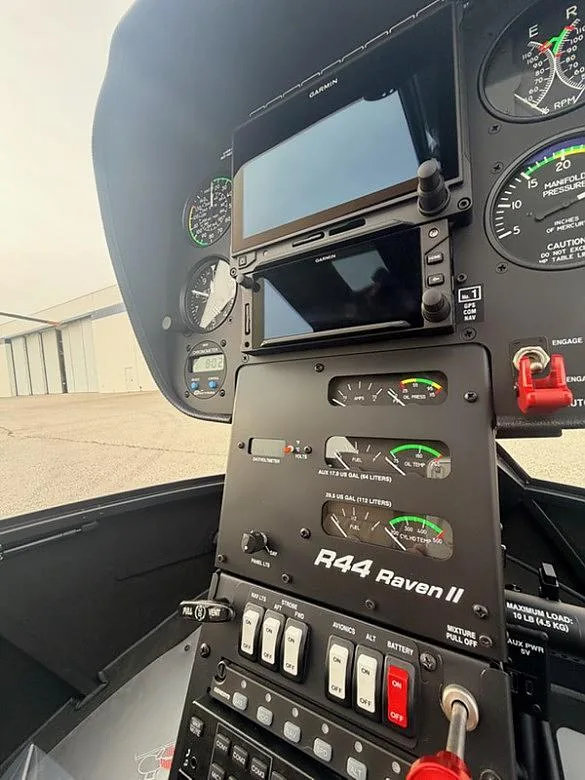 A detailed view of the instrument panel of a Robinson R44 Raven II helicopter, showing Garmin displays and gauges.