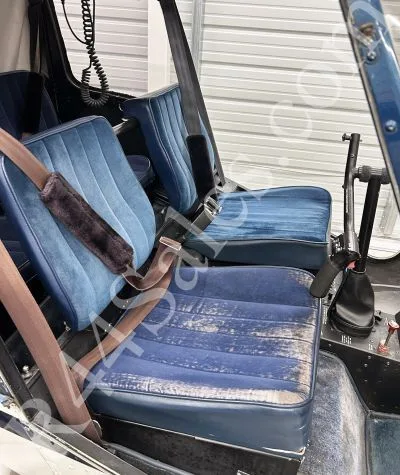 The blue fabric seats of a helicopter cabin, with visible wear on the front seat.