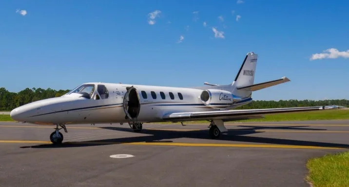 A white Cessna Citation business jet, registration N111SG, with blue and gold stripes, parked on an asphalt runway with its door open.