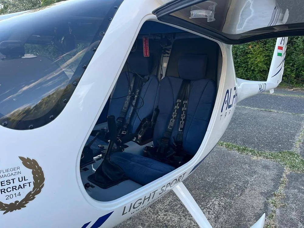 Interior view of an Alpha Light Sport aircraft cabin, showing two blue fabric seats and controls.