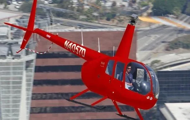 A red Robinson R44 helicopter with registration N40570 flying over a city.