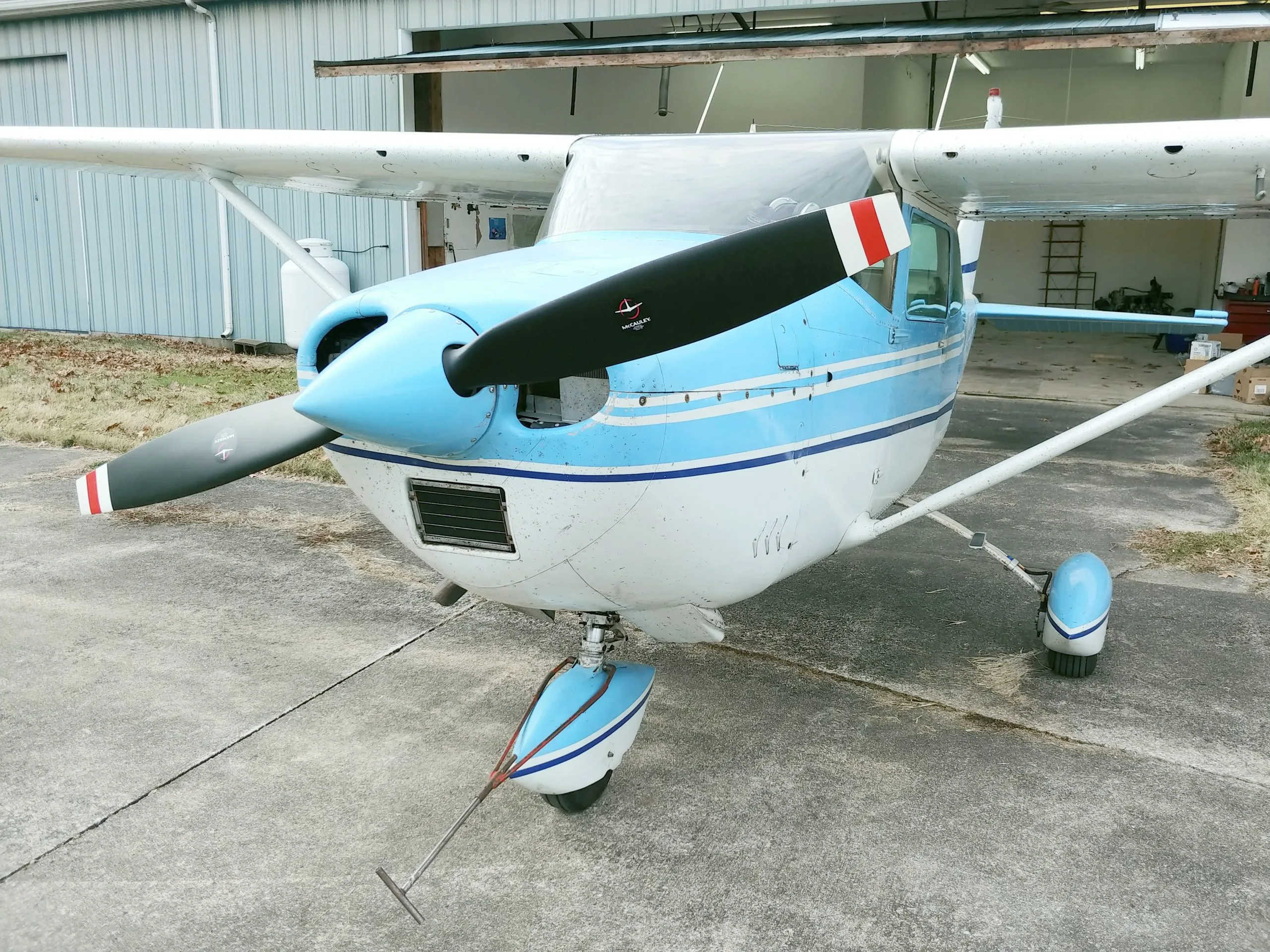 A blue and white Cessna aircraft is parked on the tarmac in front of an open hangar.