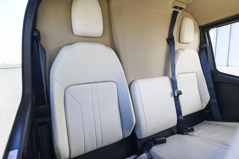 The rear cabin of a helicopter with two light-colored leather seats and tan interior trim.