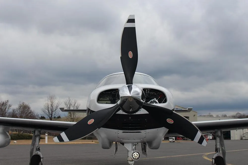 A close-up front view of the propeller and nose of a white Piper M350 aircraft under a cloudy sky.