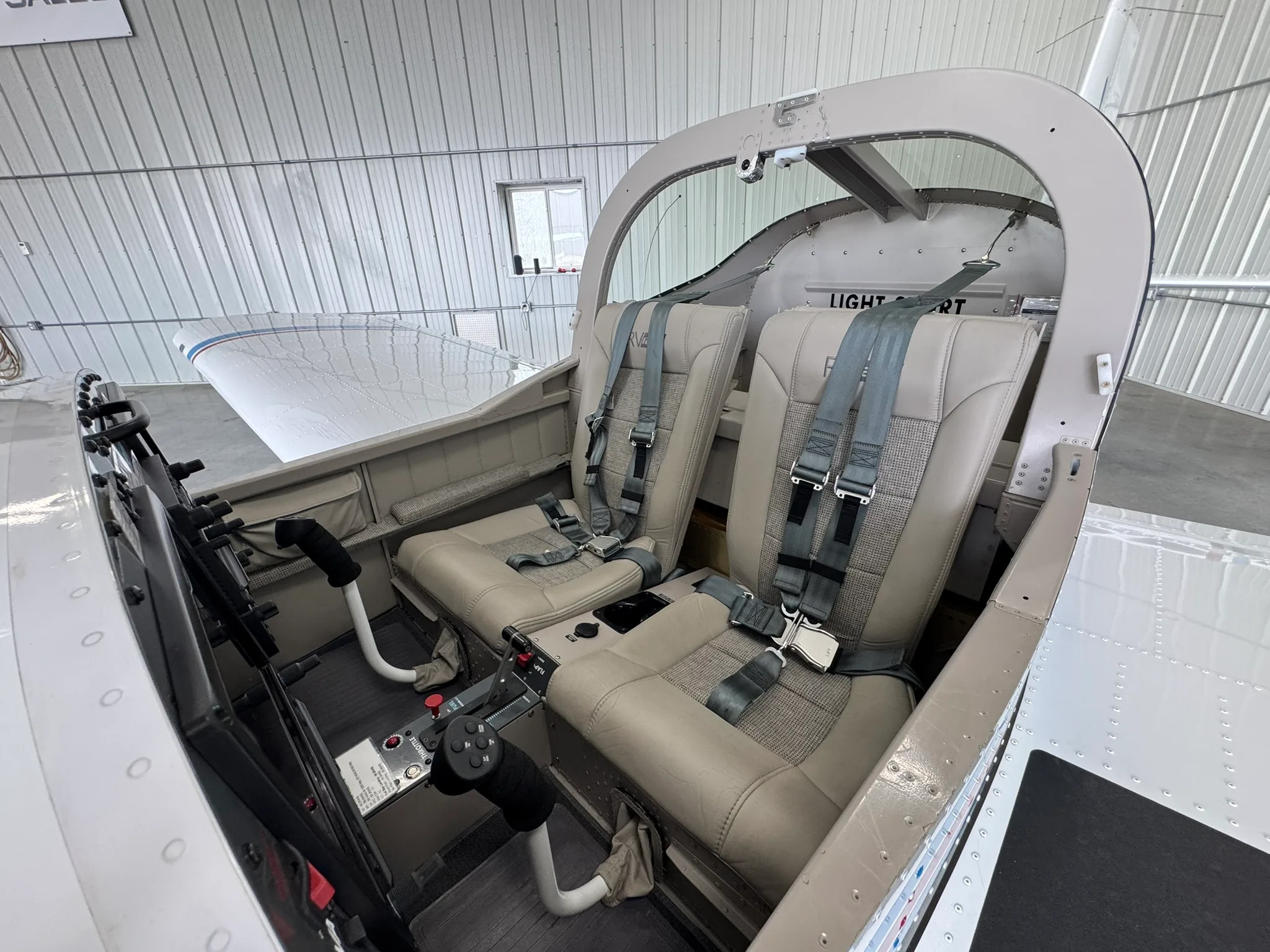 The two-seat cockpit and cabin of a light-sport aircraft, featuring beige seats and side-stick controls.