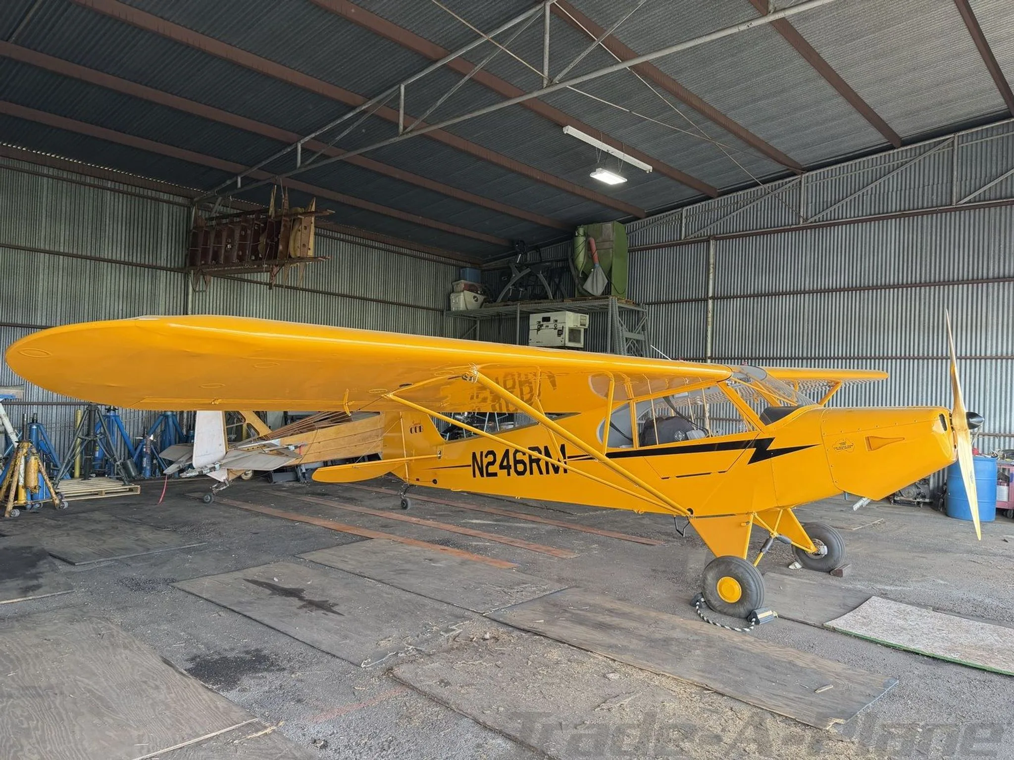 Side view of a yellow American Legend Cub aircraft with registration N246RM parked in a hangar.