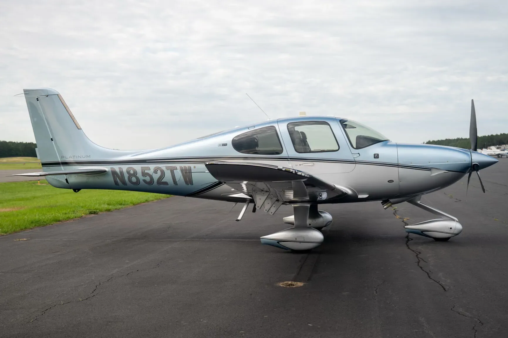 A side view of a blue and silver Cirrus SR22 aircraft, N852TW, parked on an asphalt tarmac.