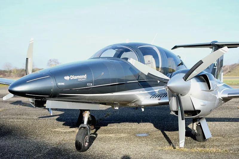 A dark grey and silver Diamond DA42 Twin Star aircraft parked on an asphalt surface.