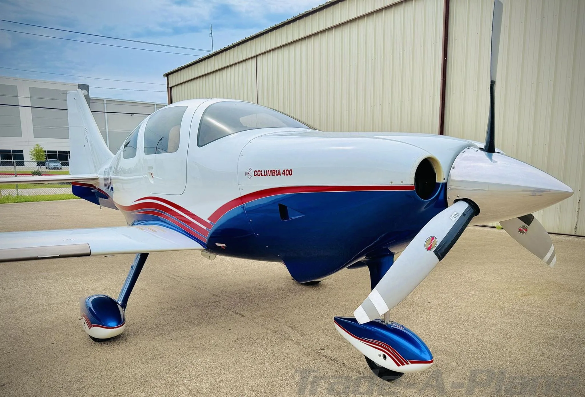 Front-right view of a white and blue Columbia 400 with red stripes on an airport apron.