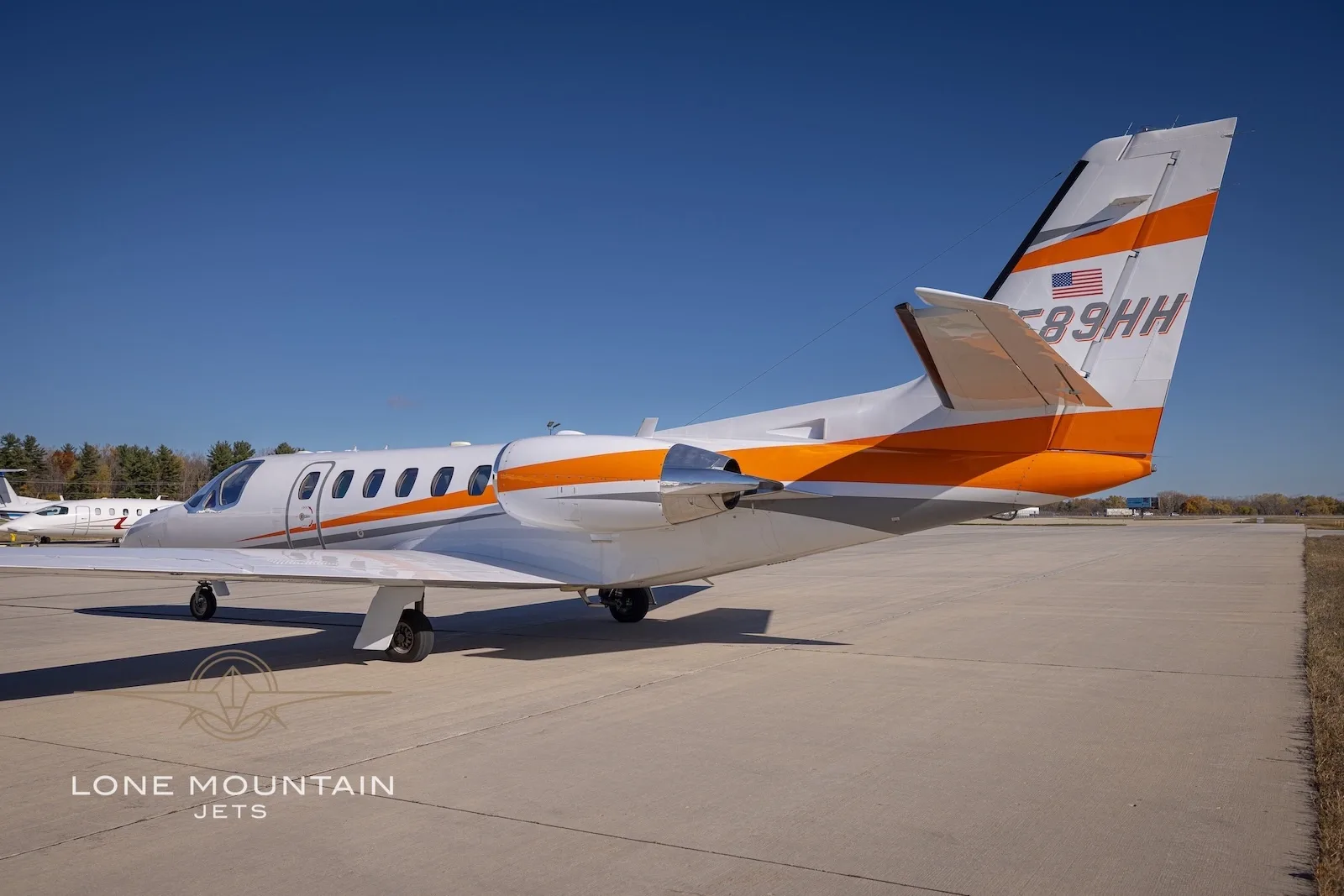 A rear quarter view of the white Cessna Citation Bravo business jet N589HH with orange and grey stripes on the tarmac.