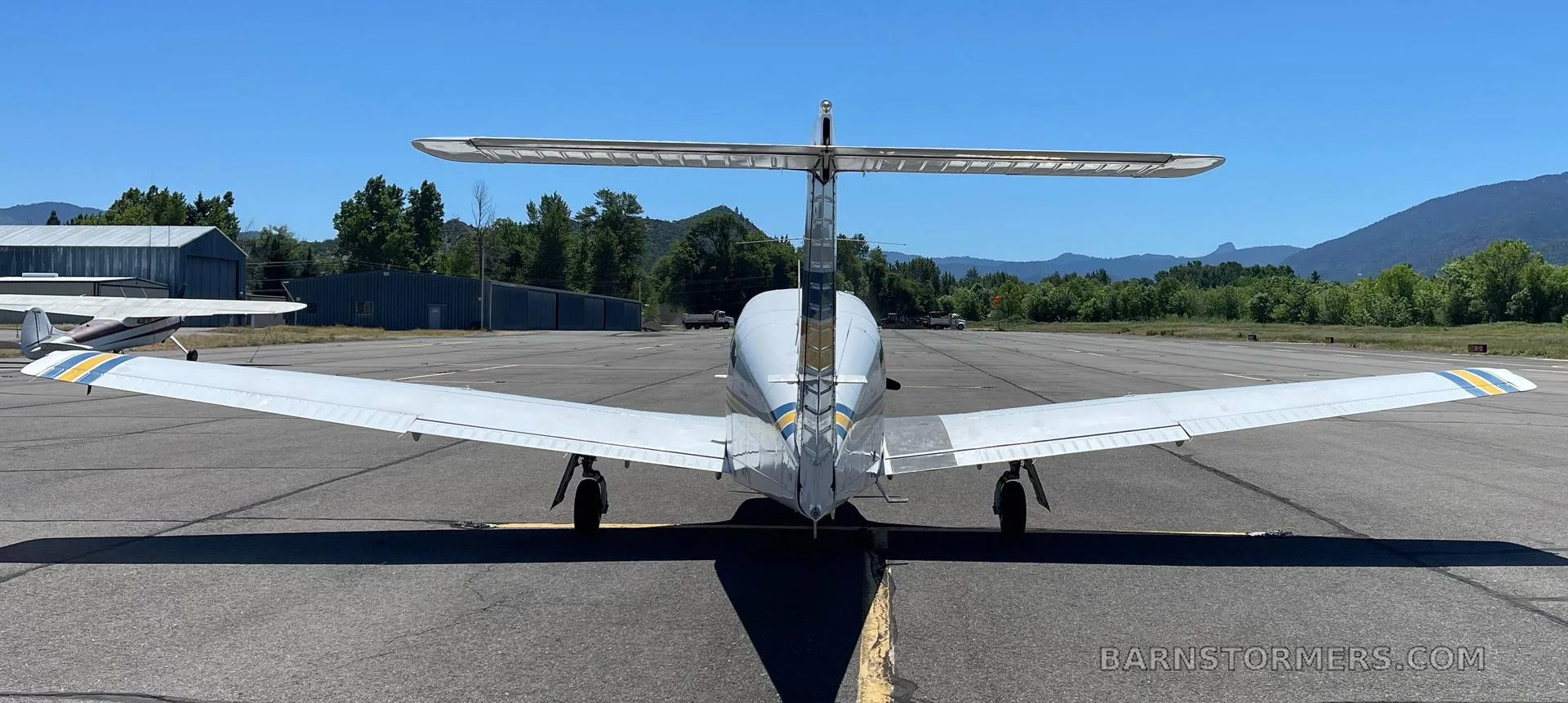 A white Piper Turbo Arrow III aircraft with blue and yellow stripes, registration N79AF, viewed from directly behind on an airfield.