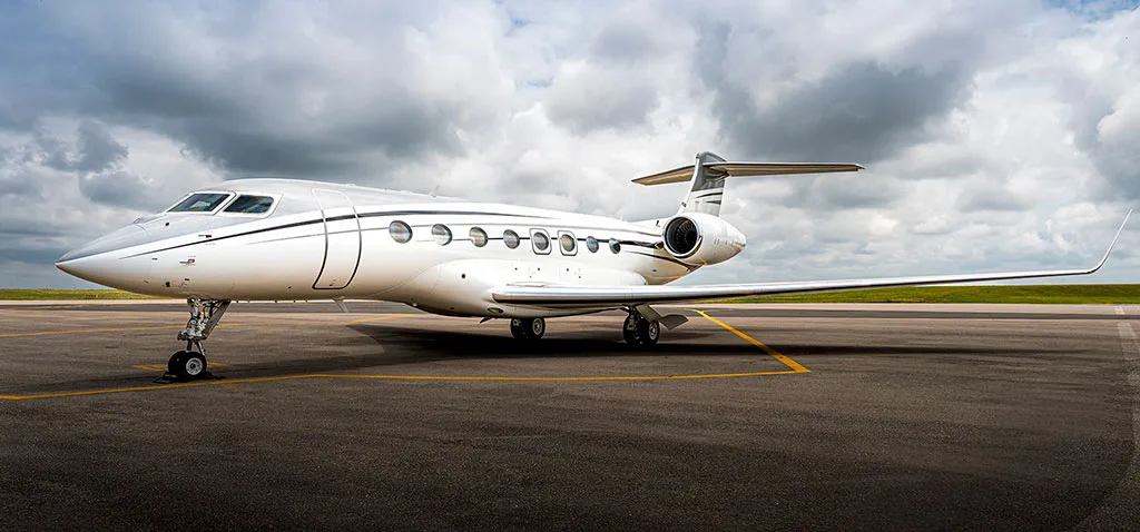 A white Gulfstream G650 business jet with black accent stripes parked on an airport tarmac under a partly cloudy sky.