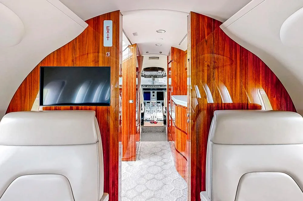 A view from the aircraft cabin looking forward towards the cockpit, featuring rich wood paneling and an 'EXIT' sign.
