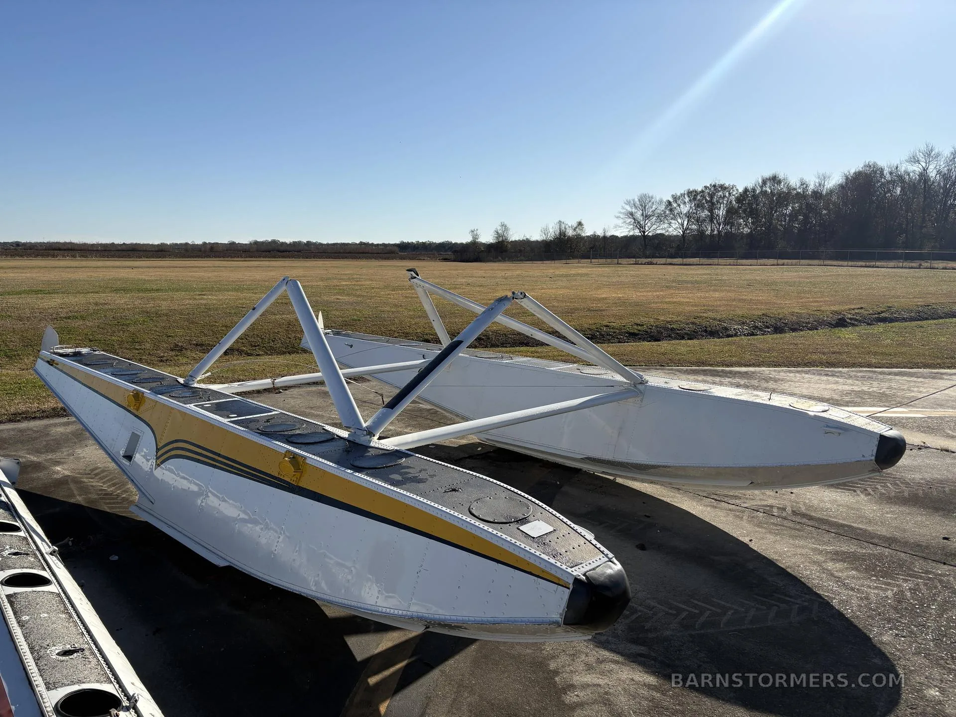 Two white aircraft floats with yellow and black stripes sit on an airfield tarmac under a clear sky.