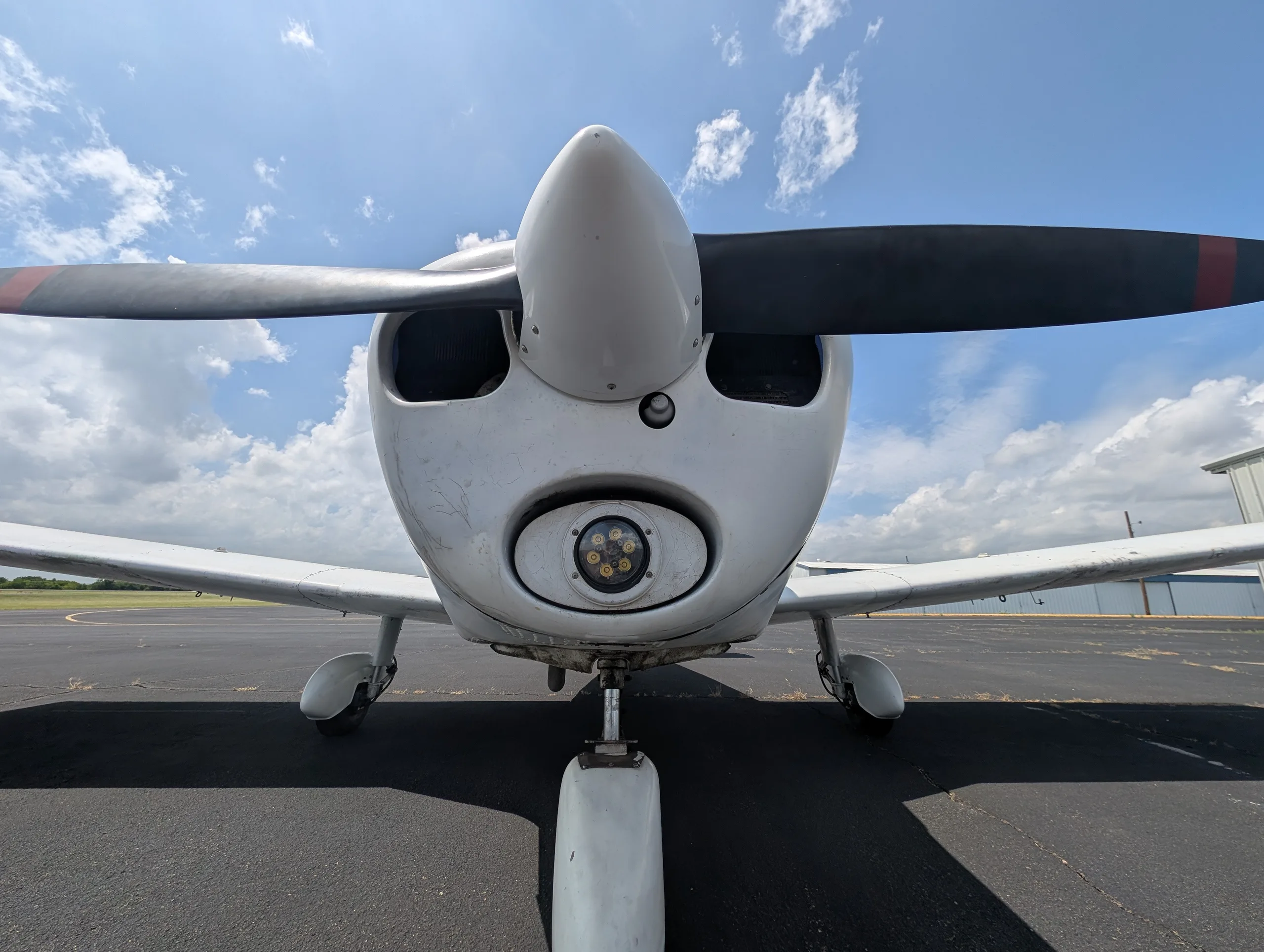 A head-on view of the white Piper Cherokee aircraft, showing the propeller and landing light.