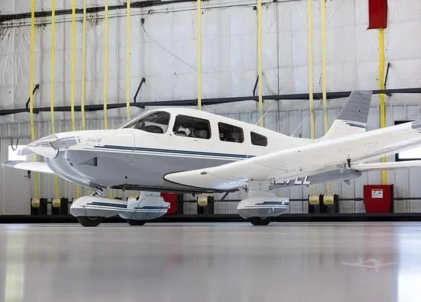 A white and grey Piper Archer III aircraft, registration N9272L, parked in a hangar, viewed from the side.