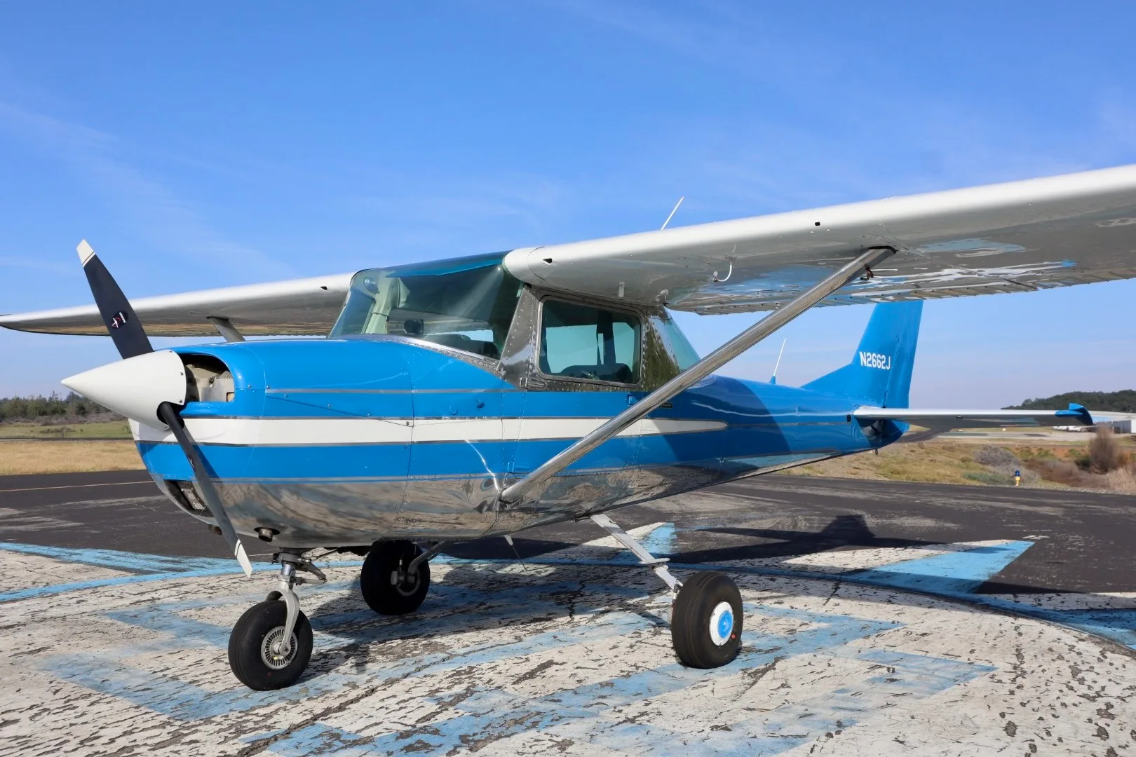 A blue and silver Cessna 150 aircraft with registration N2662J parked on an airfield.