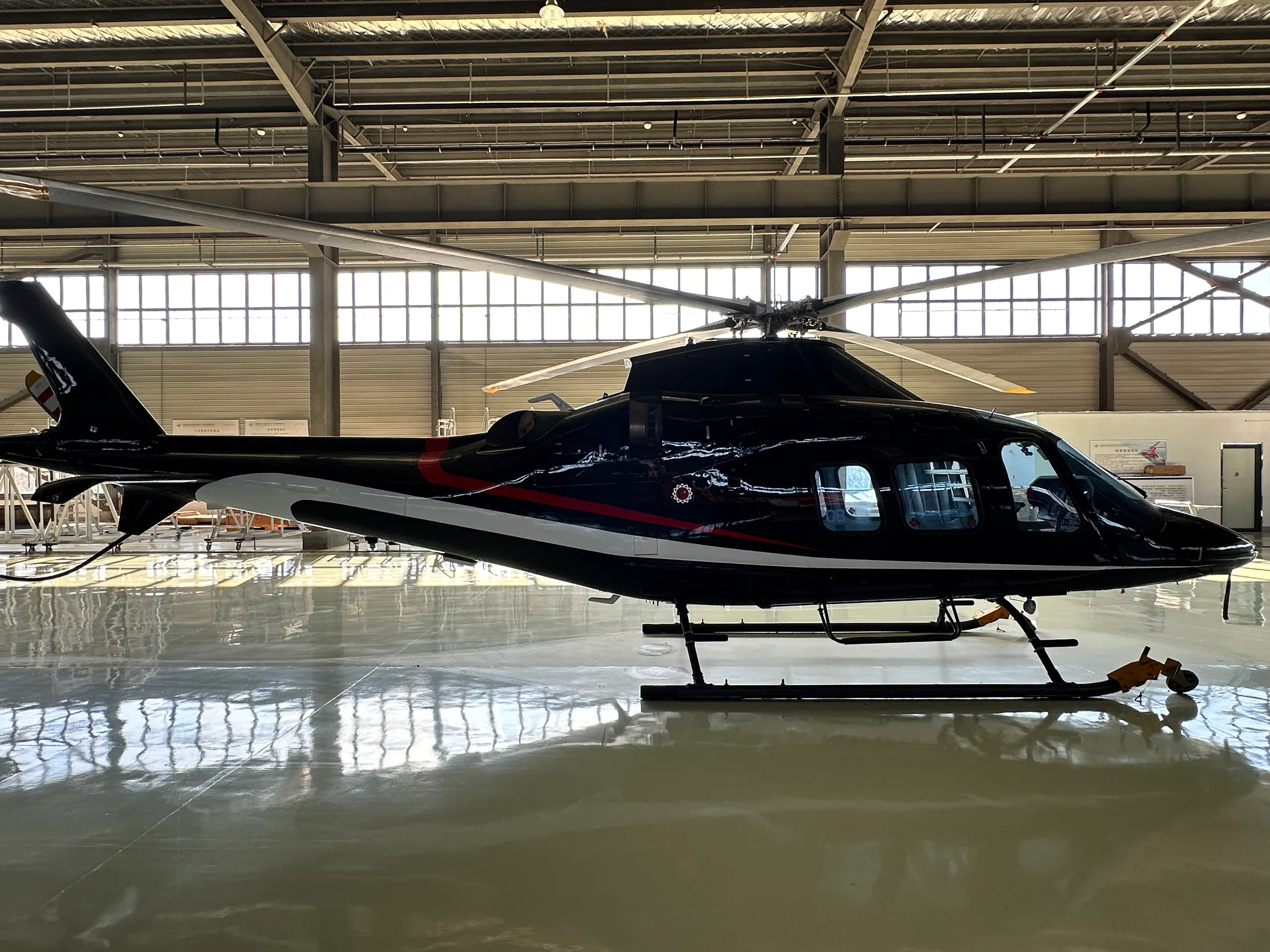 A black helicopter with white and red stripes, seen from the side, parked in a brightly lit hangar.