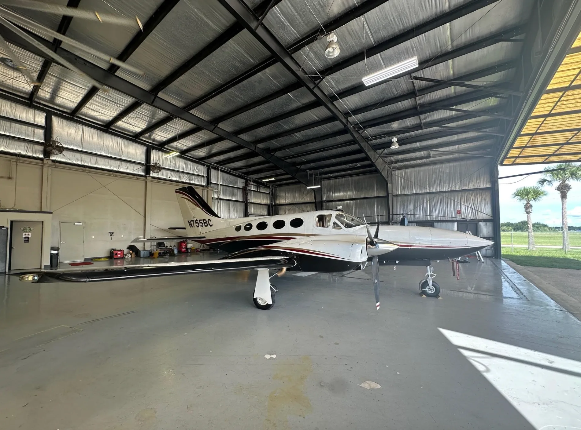 A white, black, and red twin-engine turboprop aircraft, N755BC, parked inside a hangar.
