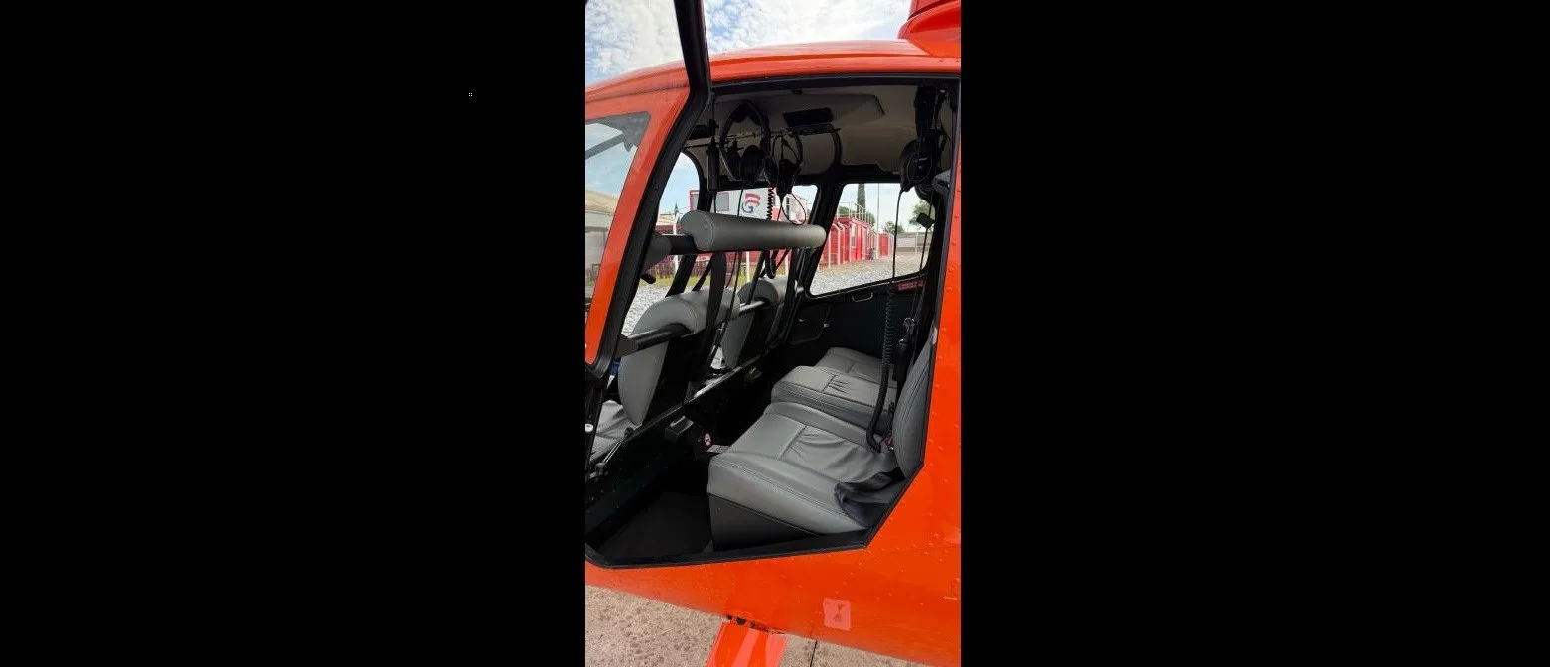 The gray interior cabin seats of an orange Robinson R66 helicopter, viewed through an open door.