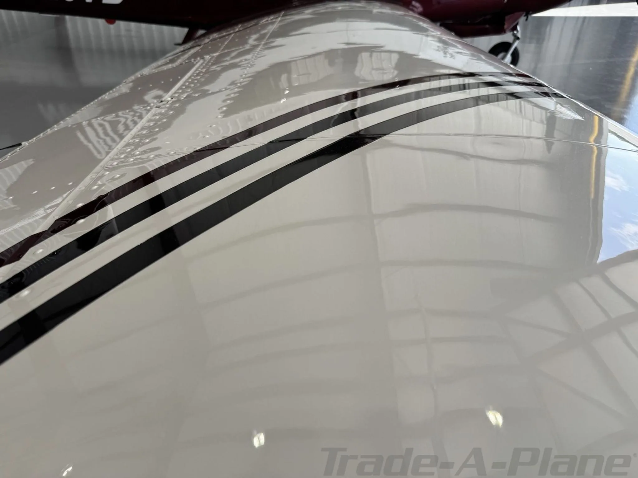 A close-up view of the white wing of a Mooney aircraft, showing black stripe details and rivets.