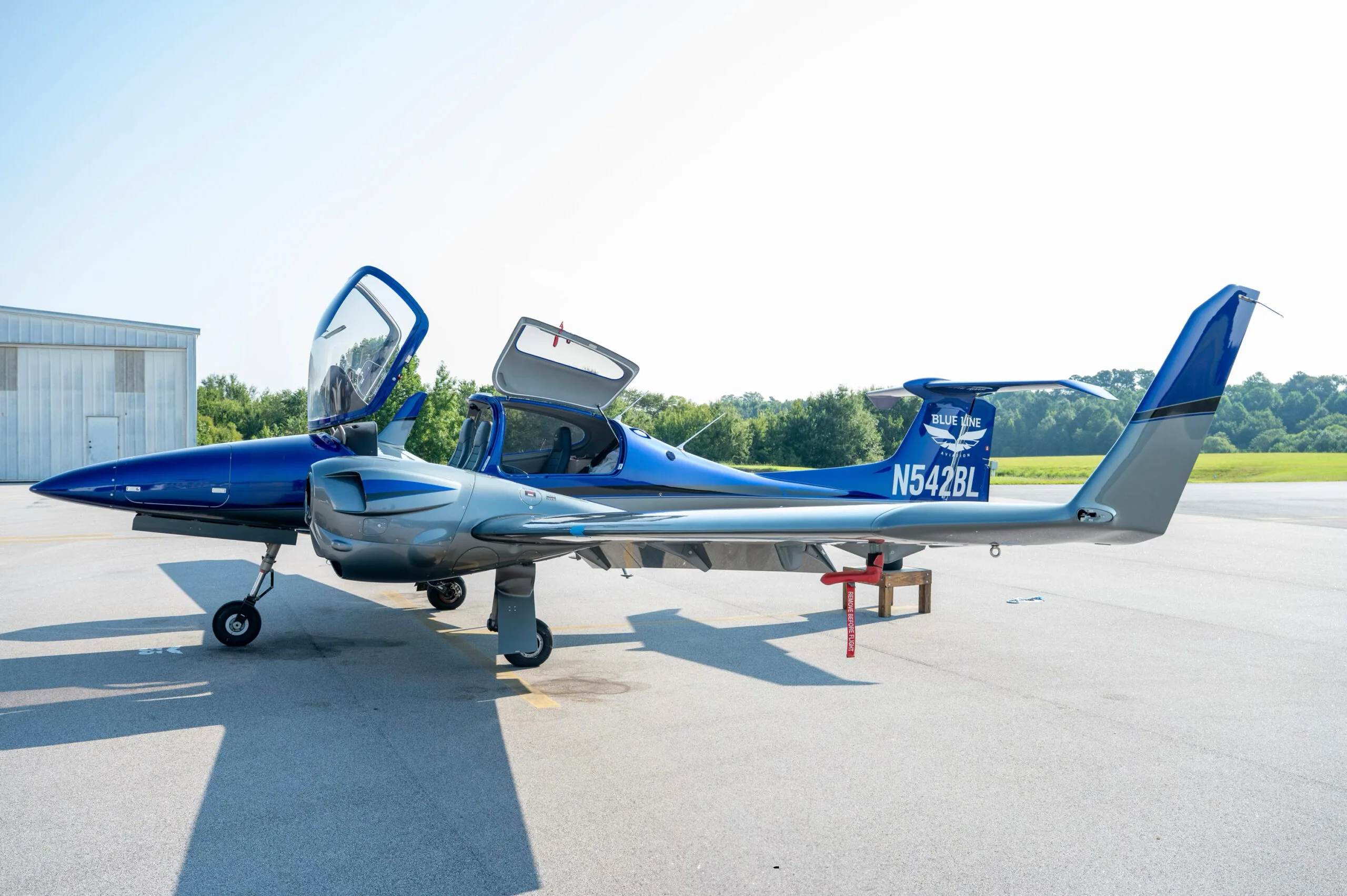 Side view of a blue and grey Diamond DA42 aircraft with doors open, parked on an airfield.