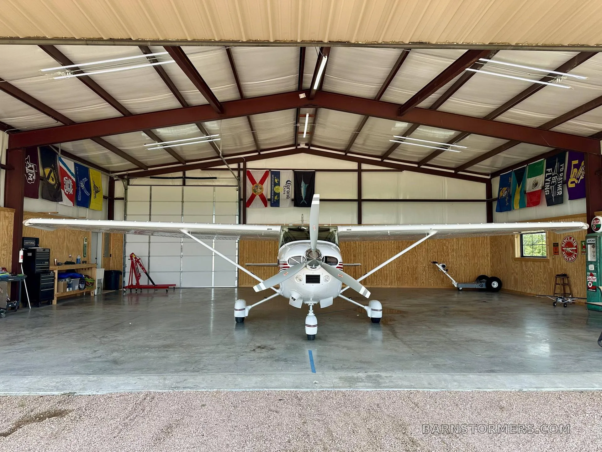 A head-on view of a white Cessna Skylane II with red stripes, parked inside a hangar with its propeller centered.