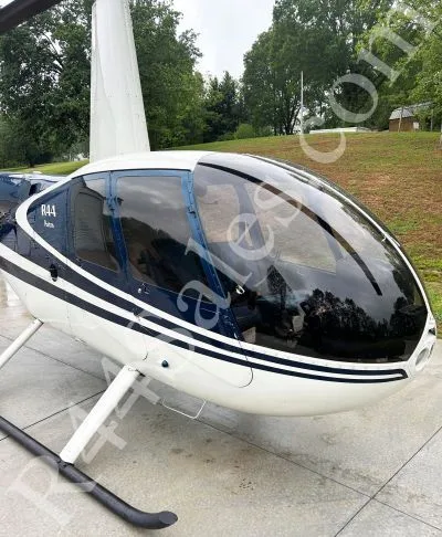 A close-up front view of a white and blue Robinson R44 helicopter on a concrete pad.