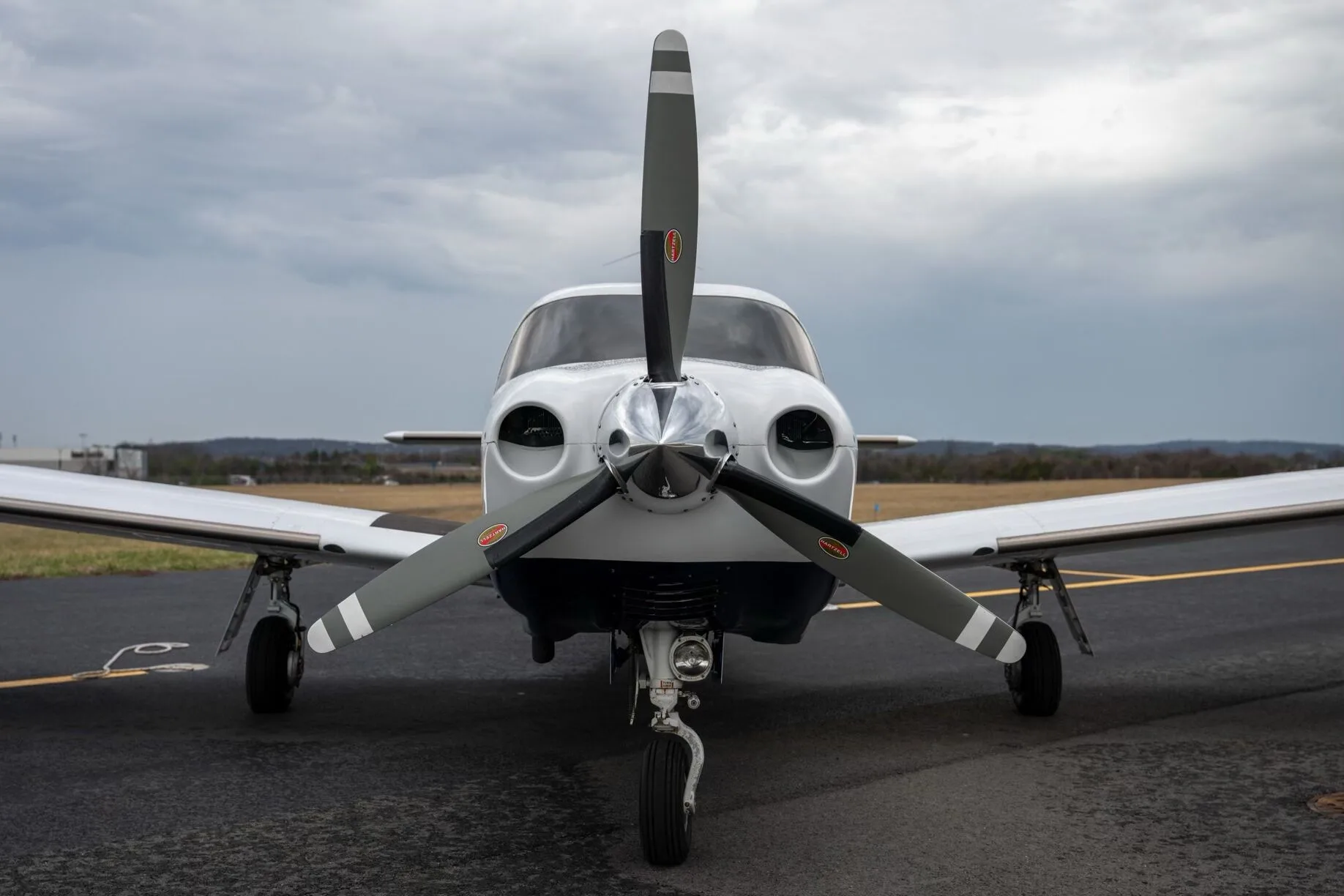 A head-on view of a white Piper Saratoga II TC aircraft, showing its propeller, nose, and landing gear on the tarmac.